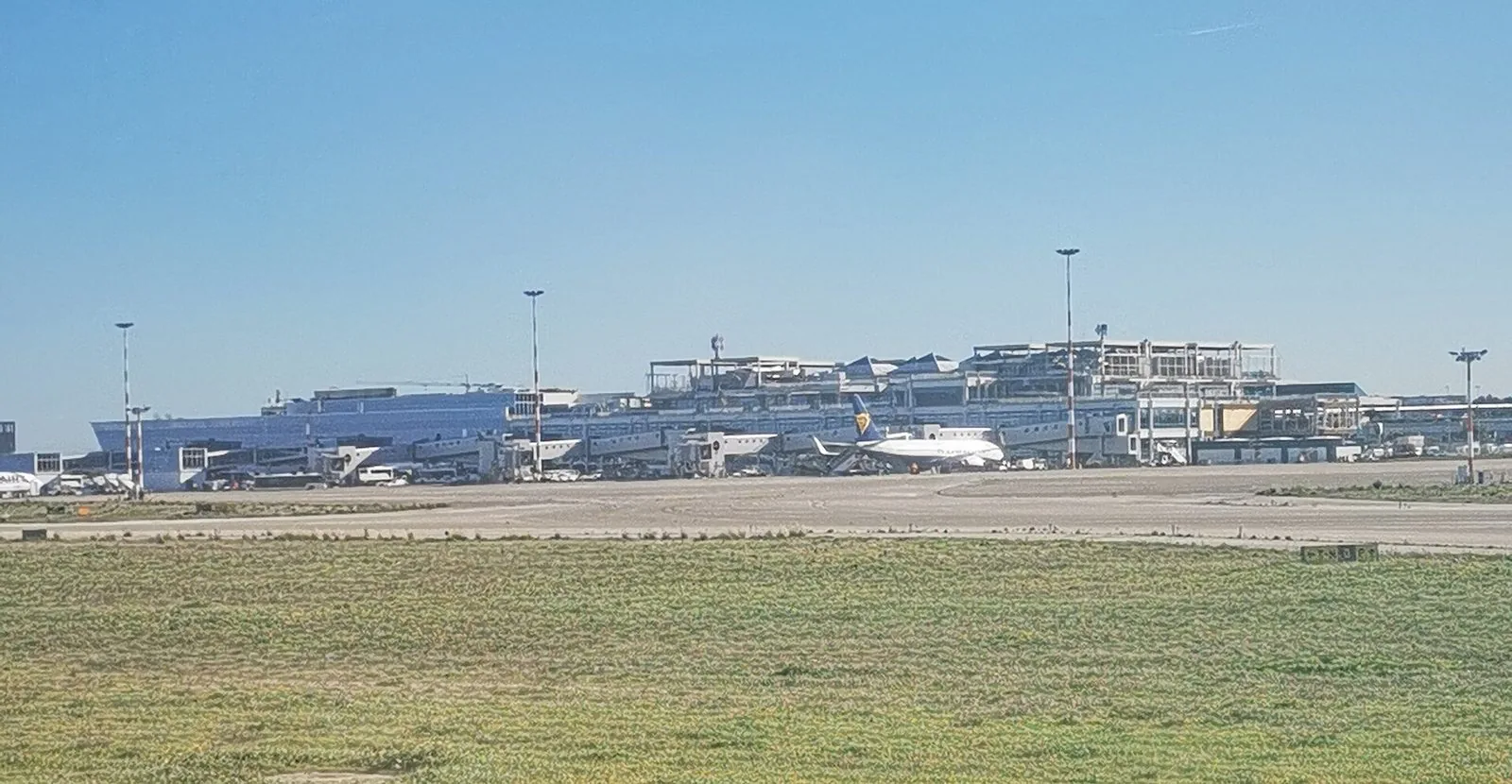 Il terminal dell'aeroporto di Bari visto dalla pista, con un aereo fermo al gate sotto un cielo azzurro
