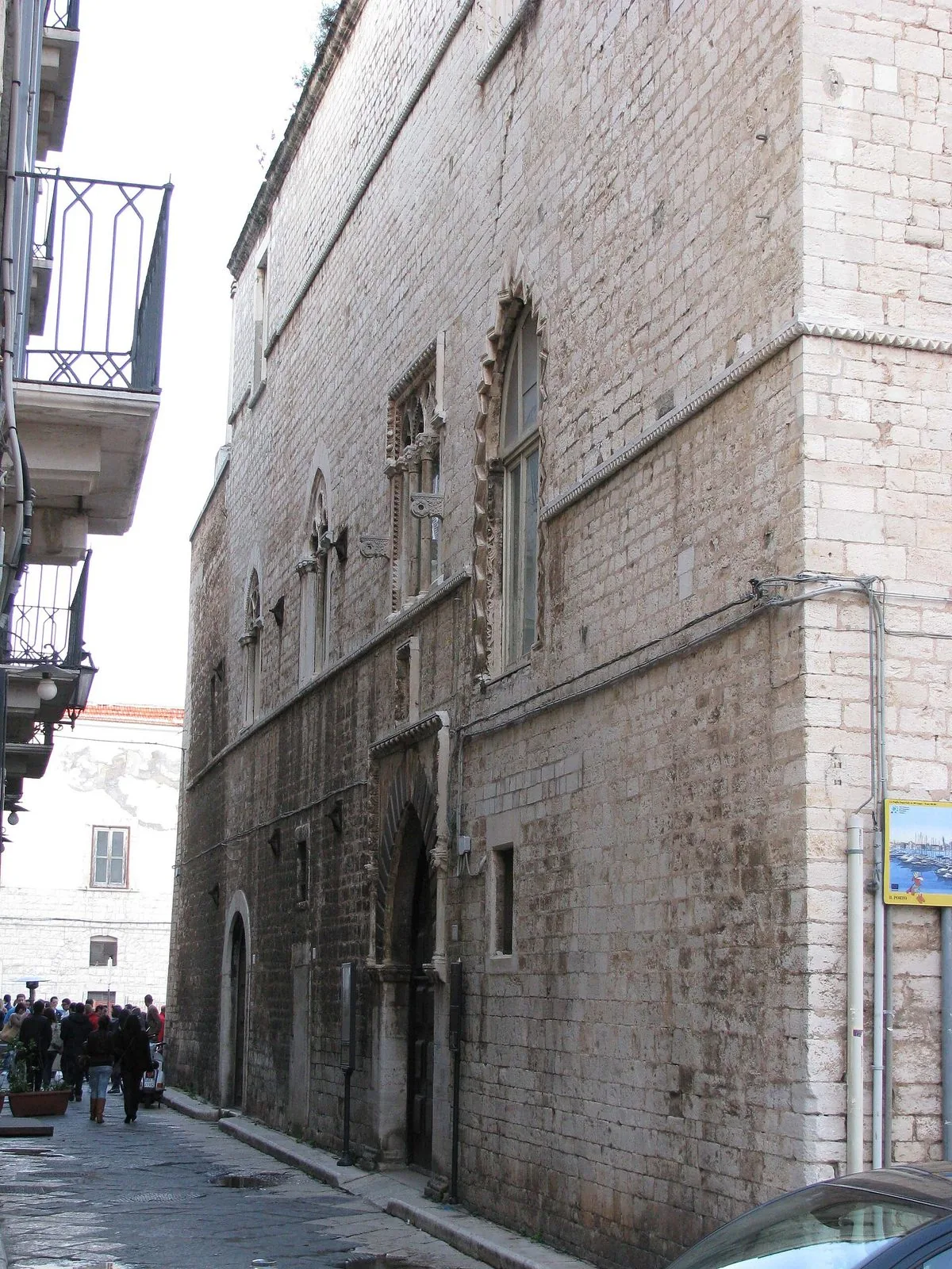 La facciata gotica di Palazzo Caccetta a Trani in una stretta via del centro storico: muro in conci di pietra chiara, finestre ad arco decorate e un portale ogivale