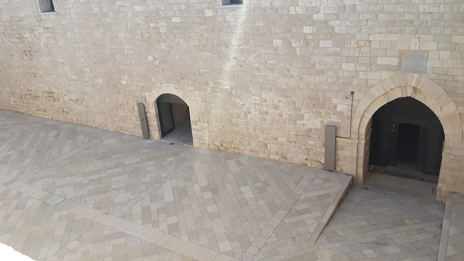 Il cortile interno del Castello Svevo di Trani visto dall'alto: pavimento in lastre di pietra chiara a spina di pesce e una parete di conci con due portali ad arco