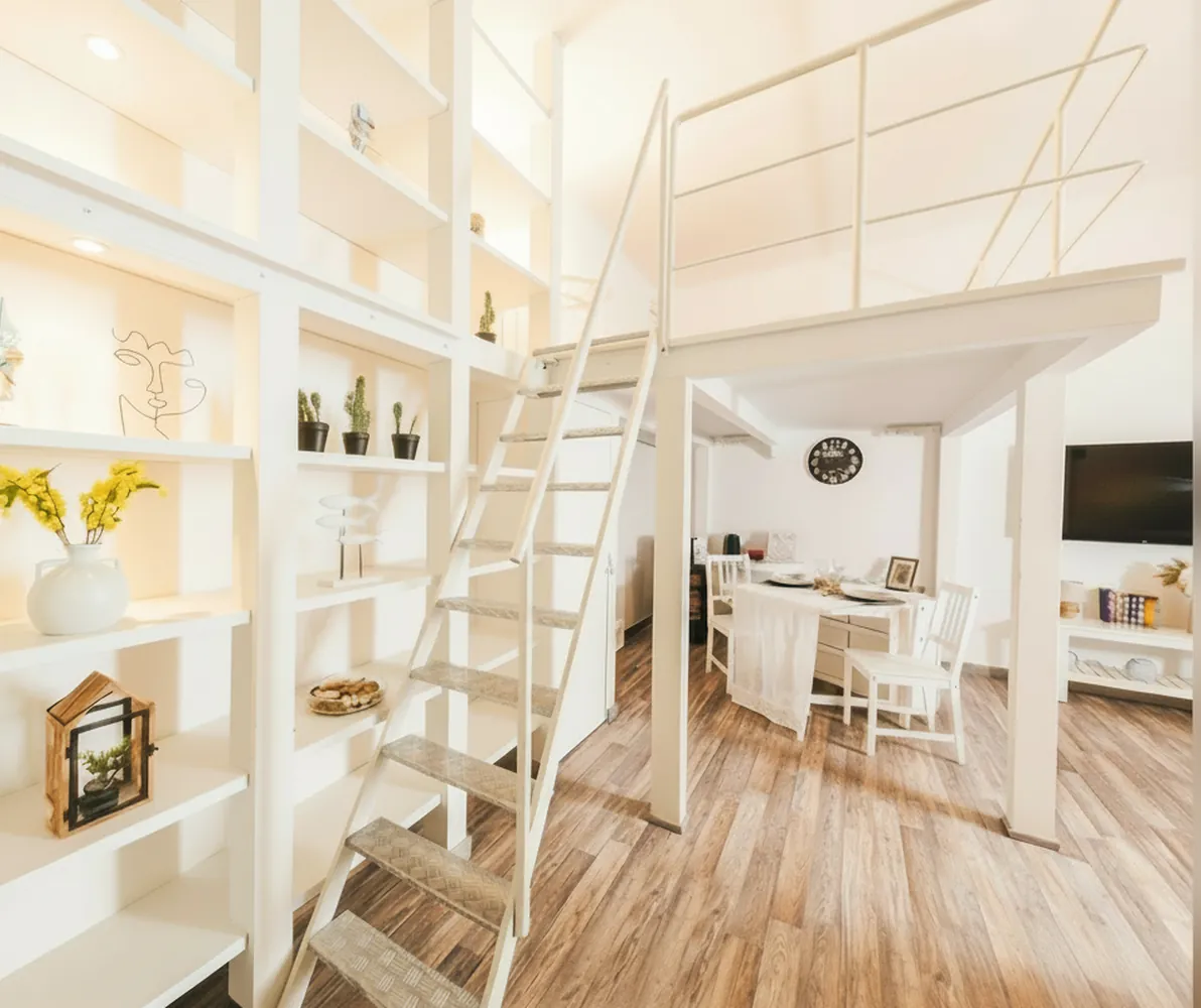 La libreria bianca con la scala del soppalco e, oltre, il tavolo e la TV della zona giorno